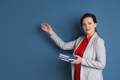 Portrait of female teacher with notebooks on color background