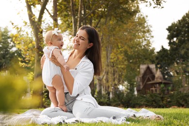 Photo of Happy mother with adorable baby sitting on green grass in park