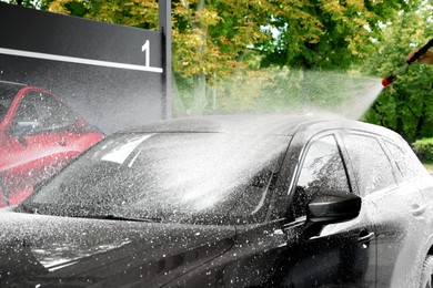 Photo of Man washing auto with high pressure water jet at outdoor car wash, closeup