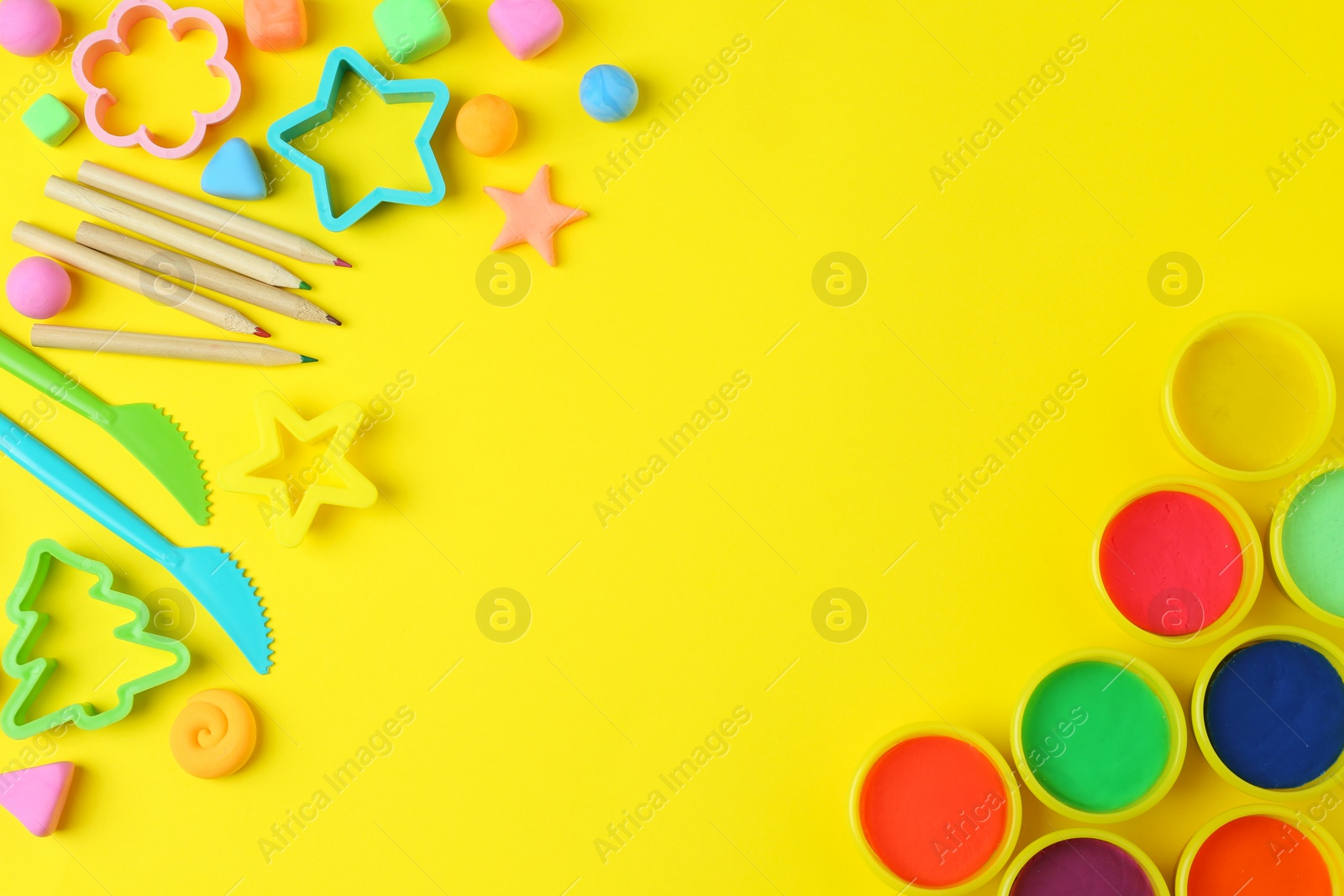 Photo of Different color play dough with tools and molds on yellow background, flat lay. Space for text