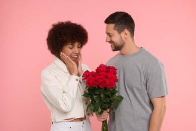 Photo of International dating. Handsome man presenting roses to his beloved woman on pink background