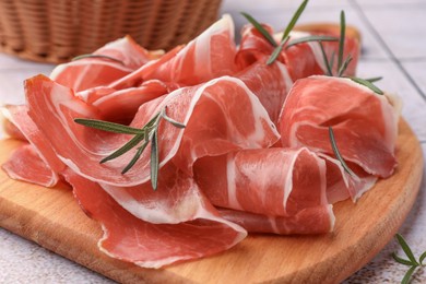 Photo of Slices of tasty cured ham and rosemary on wooden board, closeup