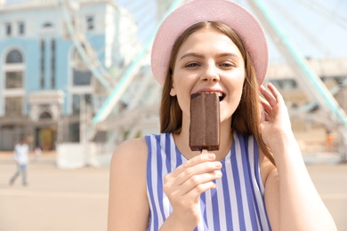 Young happy woman eating ice cream in amusement park. Space for text