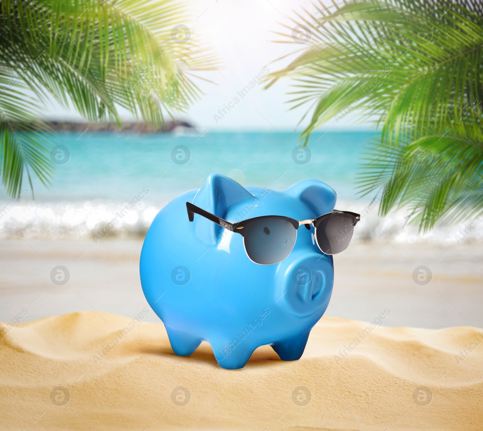 Image of Vacation savings. Piggy bank with sunglasses on sandy beach with palm trees near sea