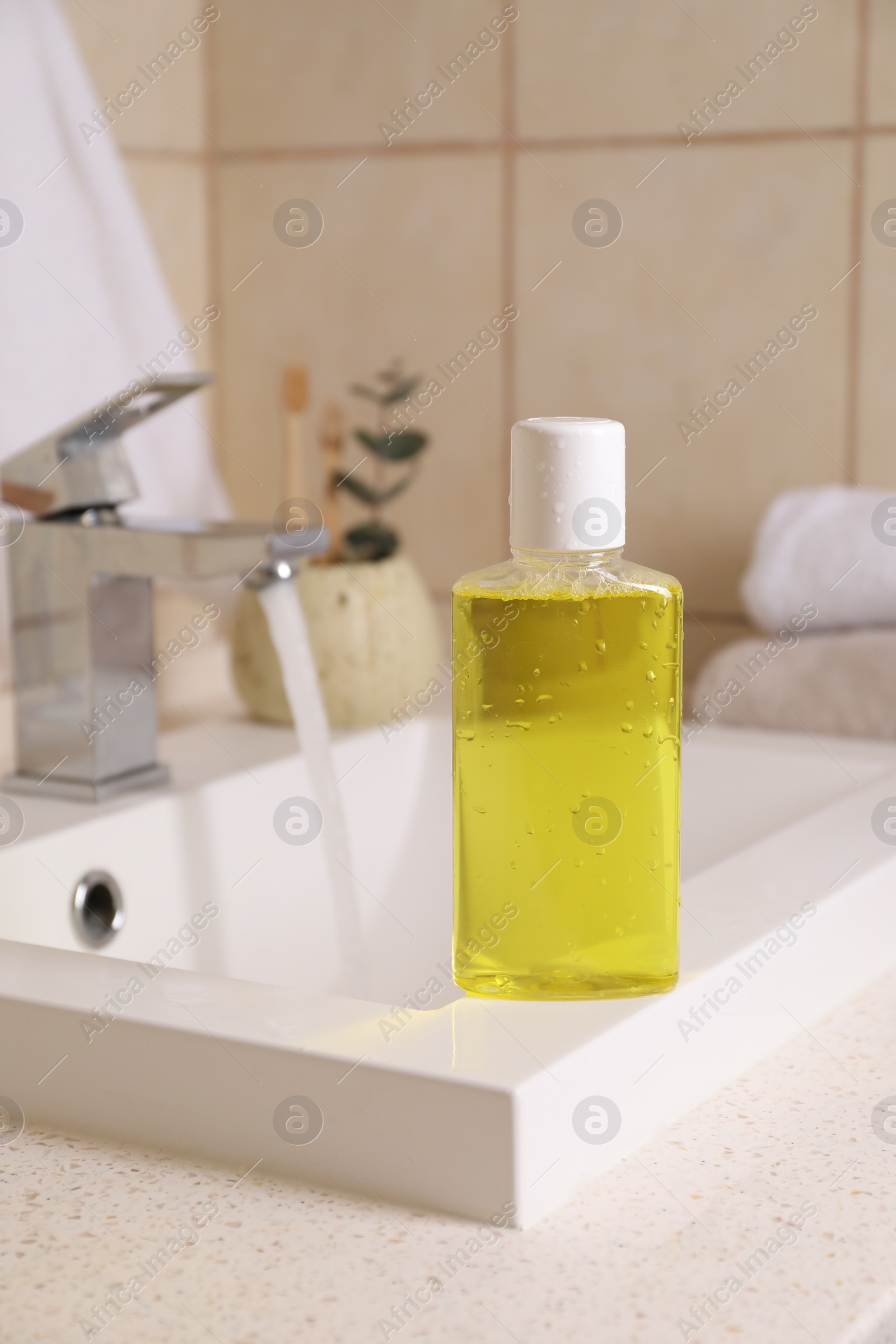 Photo of Fresh mouthwash in bottle with water drops on sink in bathroom