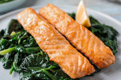 Photo of Tasty salmon with spinach and lemon on plate, closeup