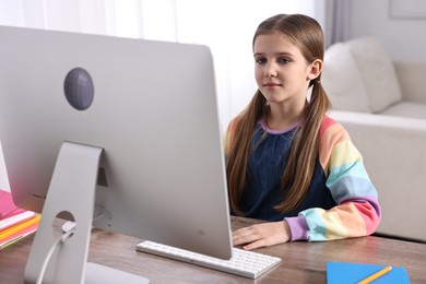 Photo of E-learning. Cute girl using computer during online lesson at table indoors