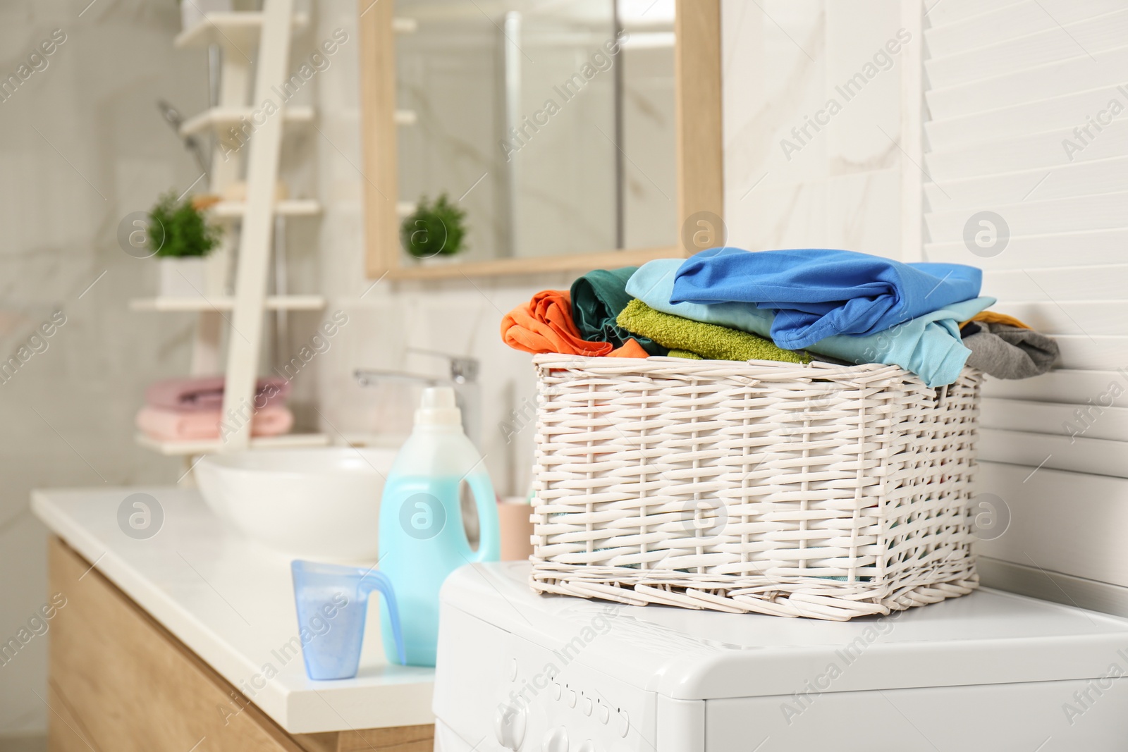 Photo of Wicker basket with laundry on washing machine in bathroom