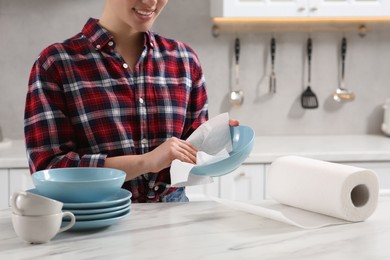 Photo of Woman wiping bowl with paper towel at white marble table in kitchen, closeup