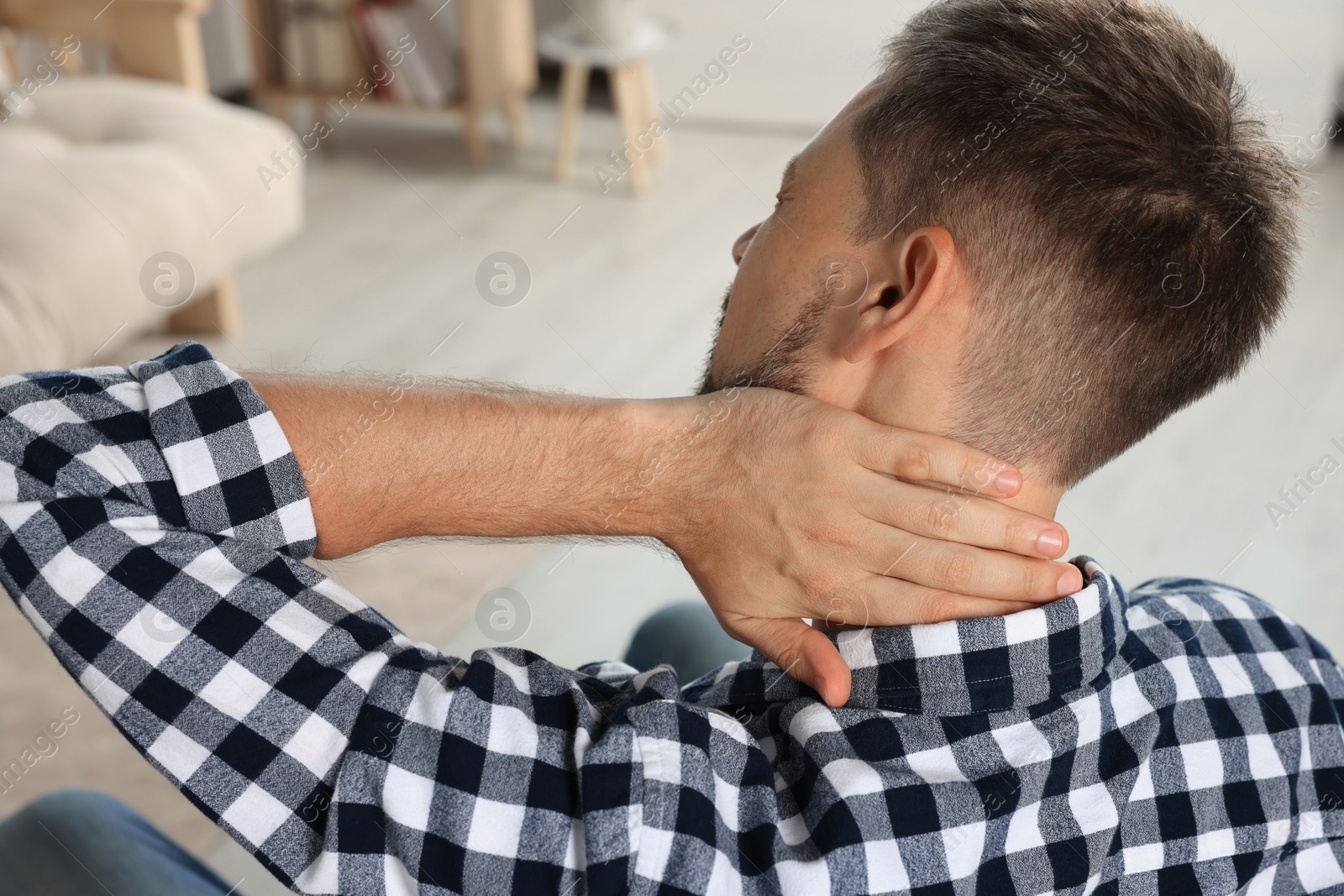 Photo of Man suffering from neck pain indoors, back view