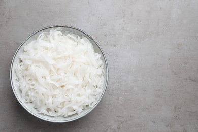 Photo of Bowl with cooked rice noodles on light grey table, top view. Space for text