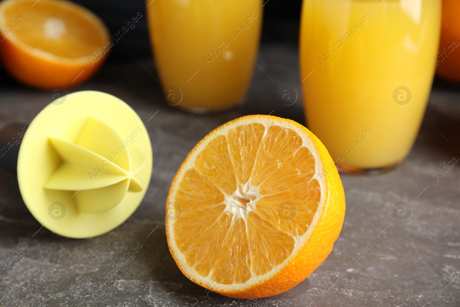 Photo of Cut fresh ripe orange, reamer and juice on grey table, closeup