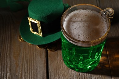 Photo of St. Patrick's day party. Green beer, leprechaun hat and gold on wooden table, closeup. Space for text