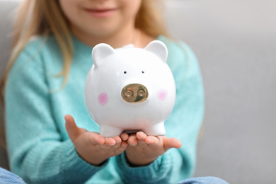 Photo of Girl holding piggy bank on light background, closeup