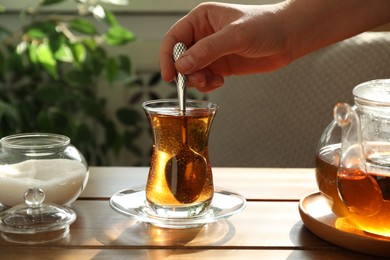 Photo of Woman stirring sugar in tea at wooden table indoors, closeup