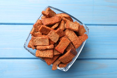 Photo of Crispy rye rusks in bowl on light blue wooden table, top view