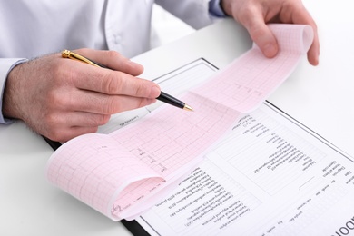 Doctor examining cardiogram at table in clinic, closeup
