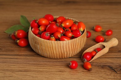 Photo of Ripe rose hip berries with green leaves on wooden table