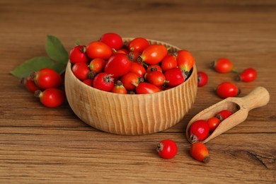 Ripe rose hip berries with green leaves on wooden table