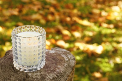 Photo of Burning candle on wooden surface outdoors, space for text. Autumn atmosphere