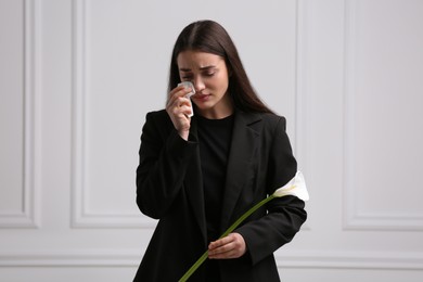 Sad woman with calla lily flower mourning near white wall. Funeral ceremony