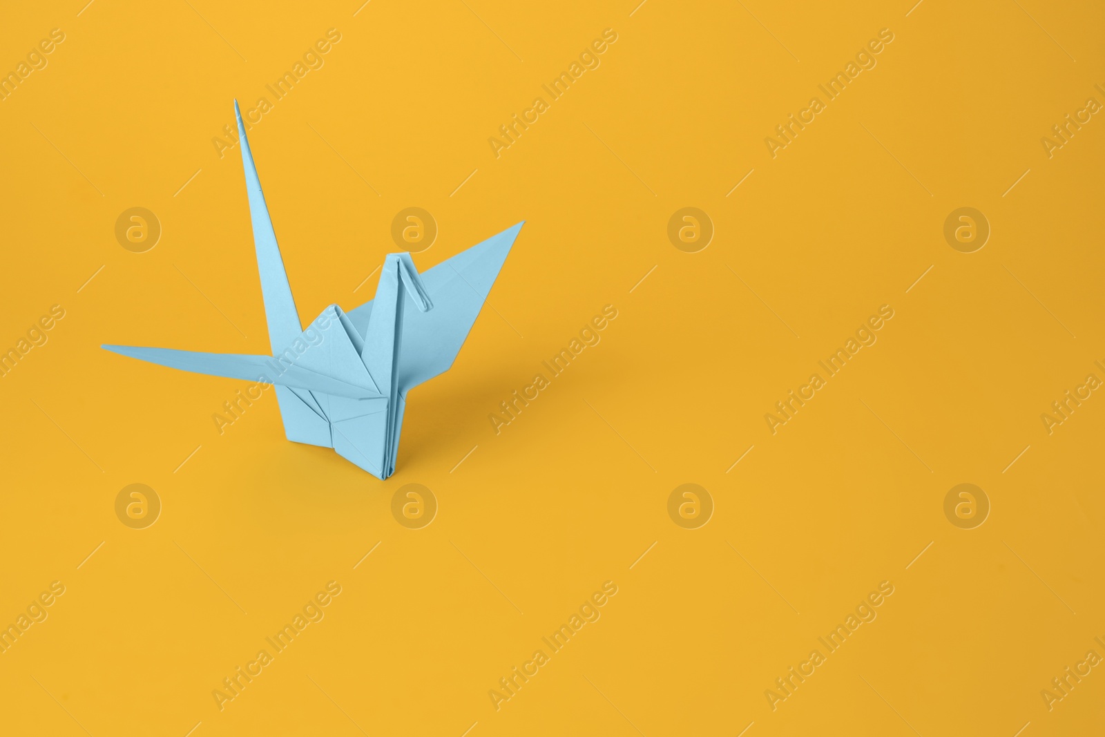 Photo of Origami art. Beautiful light blue paper crane on orange background, space for text