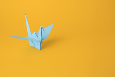 Origami art. Beautiful light blue paper crane on orange background, space for text