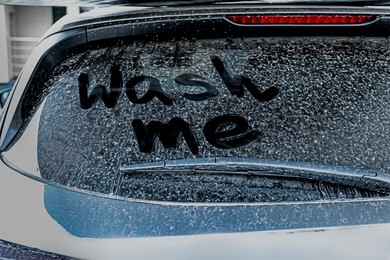 Photo of Phrase Wash Me written on dirty car window outdoors, closeup