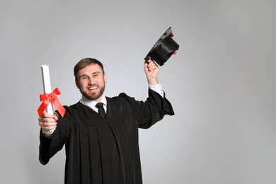 Photo of Happy student with graduation hat and diploma on grey background. Space for text