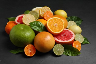 Photo of Different ripe citrus fruits with green leaves on black table