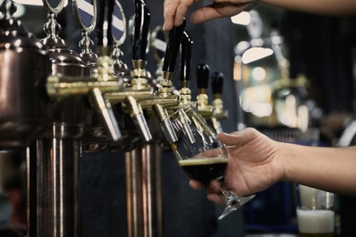 Bartender pouring beer into glass in pub, closeup