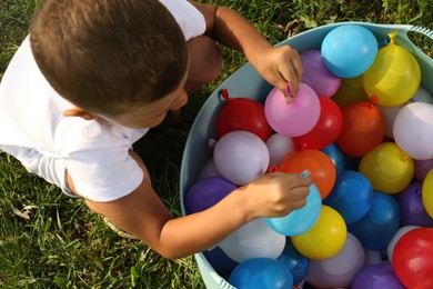 Photo of Little boy with basin of water bombs on green grass, top view