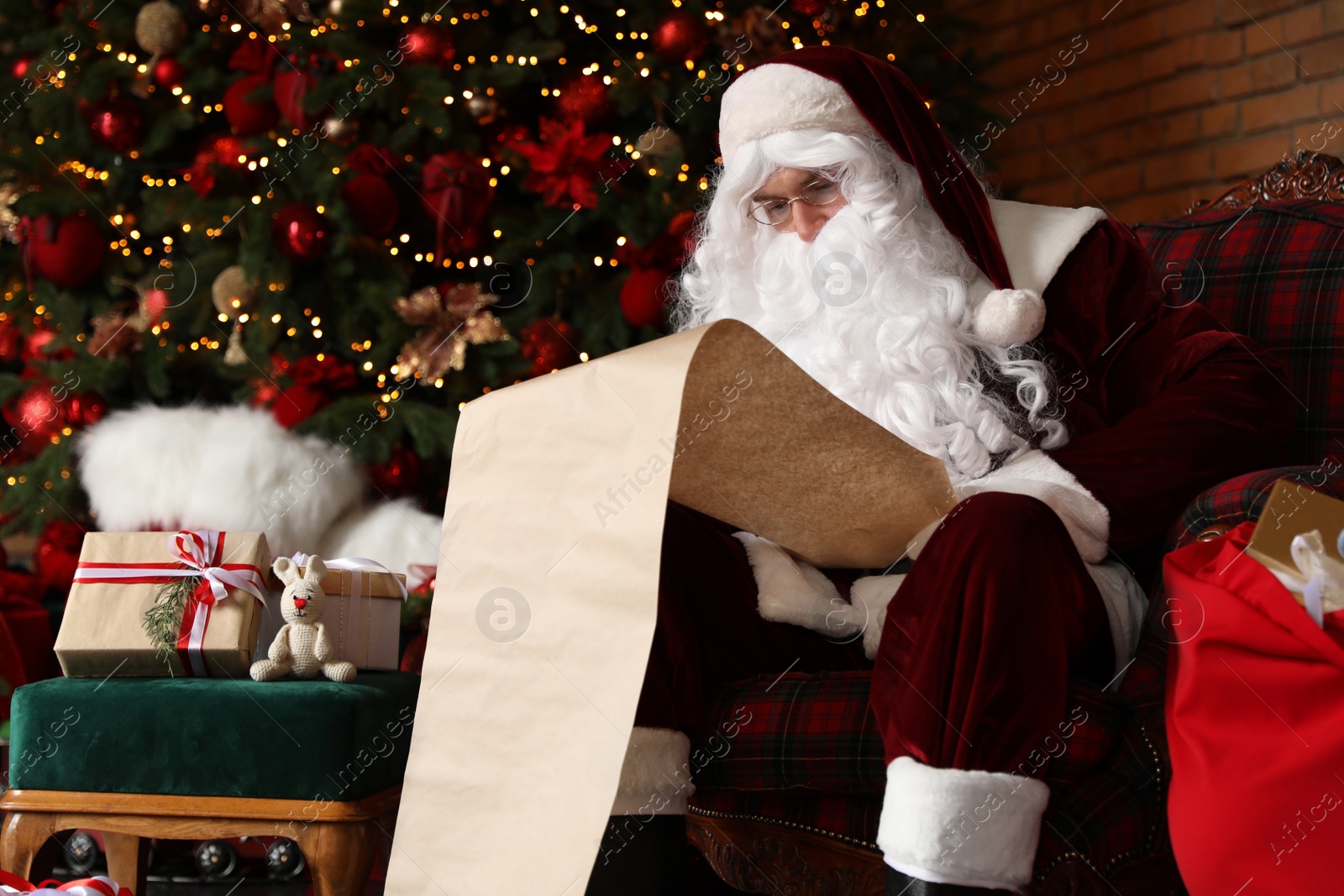Photo of Santa Claus reading wish list in armchair near Christmas tree