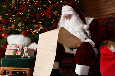 Santa Claus reading wish list in armchair near Christmas tree