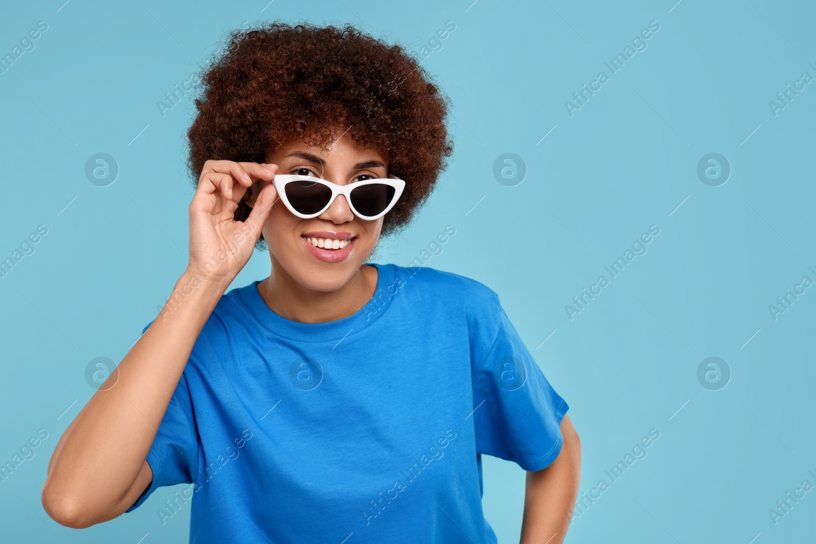 Photo of Happy young woman in stylish sunglasses on light blue background. Space for text