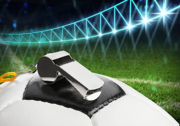 Image of Referee equipment. Soccer ball and whistle on green football field under stadium lights, closeup