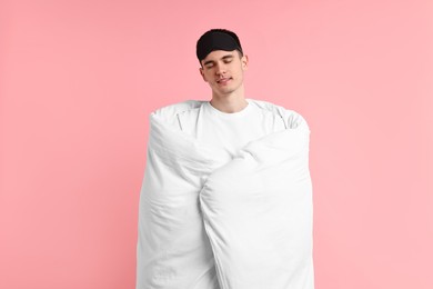 Photo of Man in pyjama and sleep mask wrapped in blanket on pink background