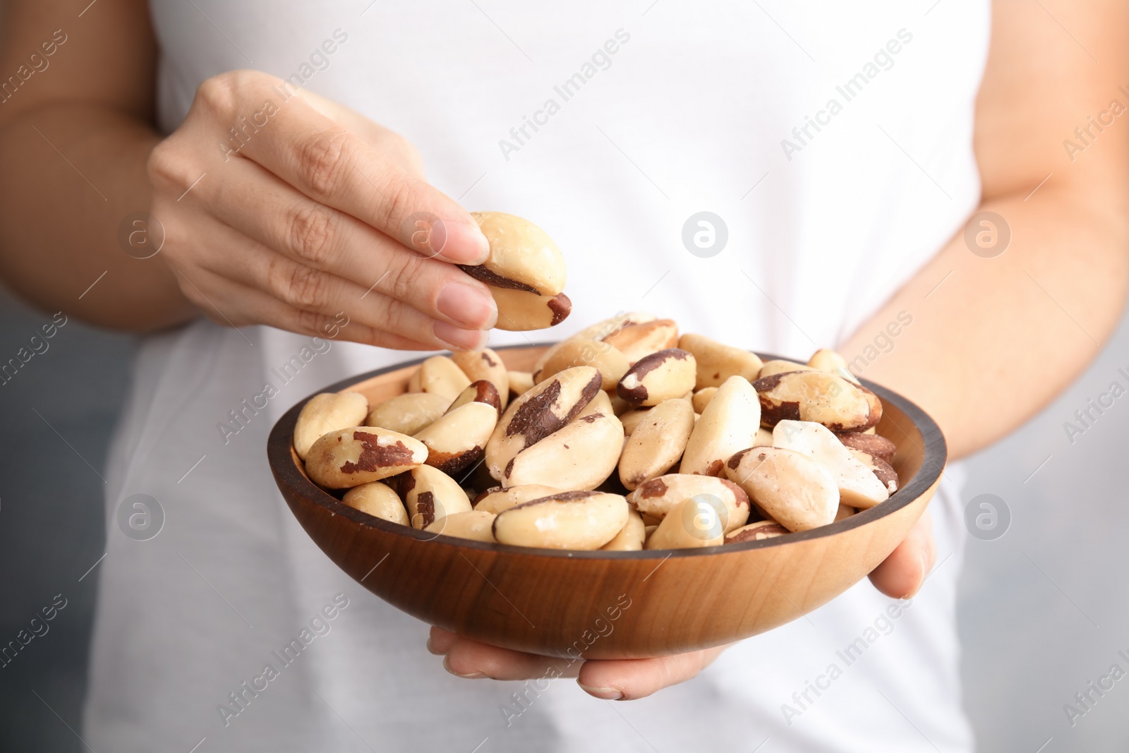 Photo of Woman holding bowl with Brazil nuts on grey background, closeup