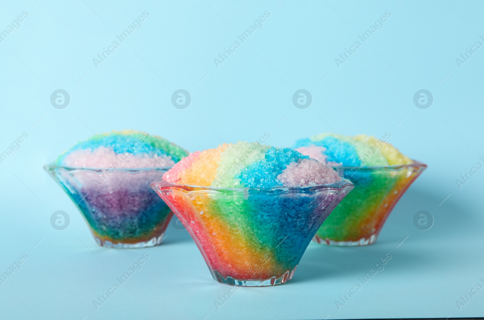 Photo of Rainbow shaving ice in glass dessert bowls on light blue background