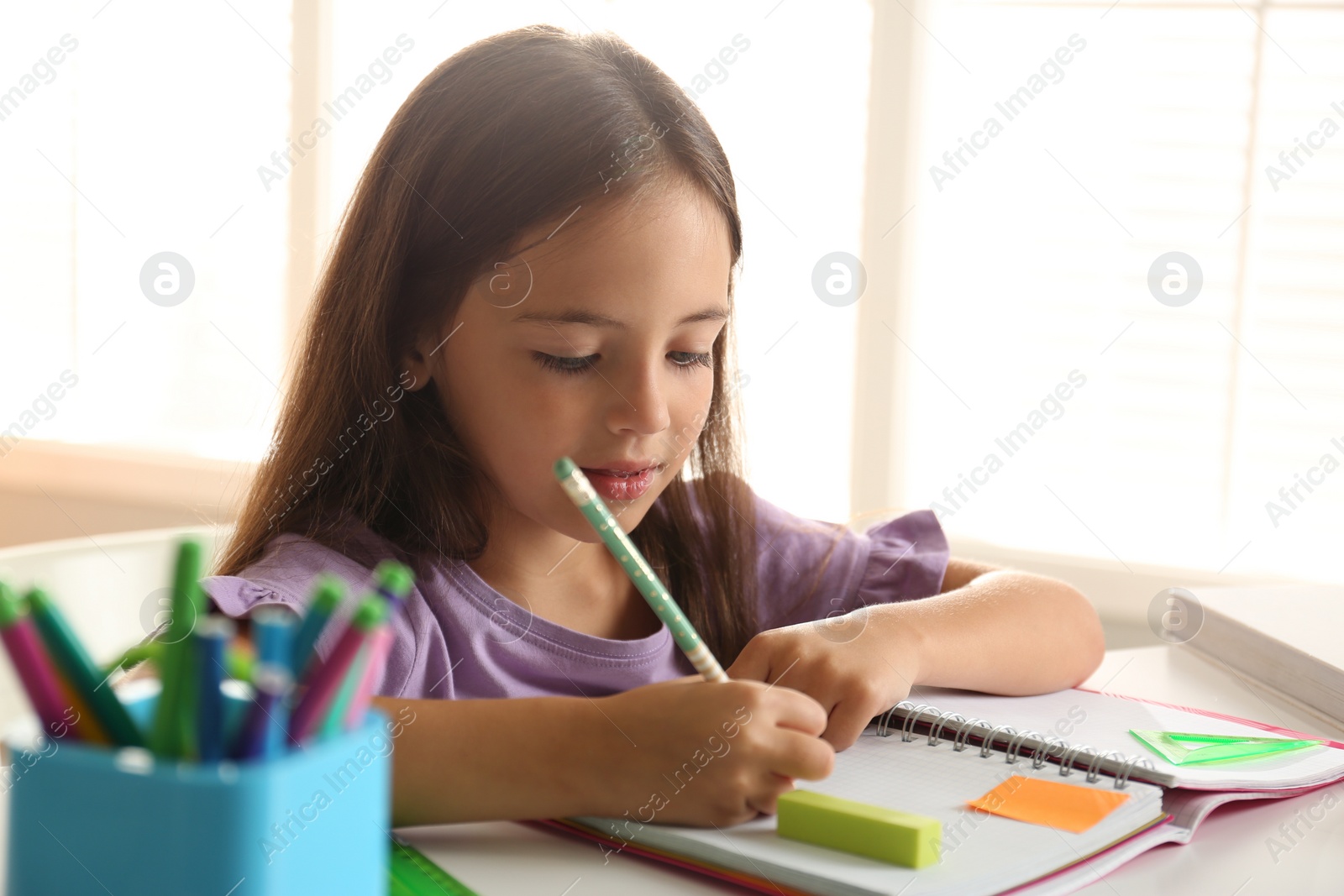 Photo of Little girl doing homework at table indoors