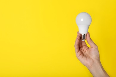 Photo of Woman holding LED light bulb on yellow background, closeup. Space for text
