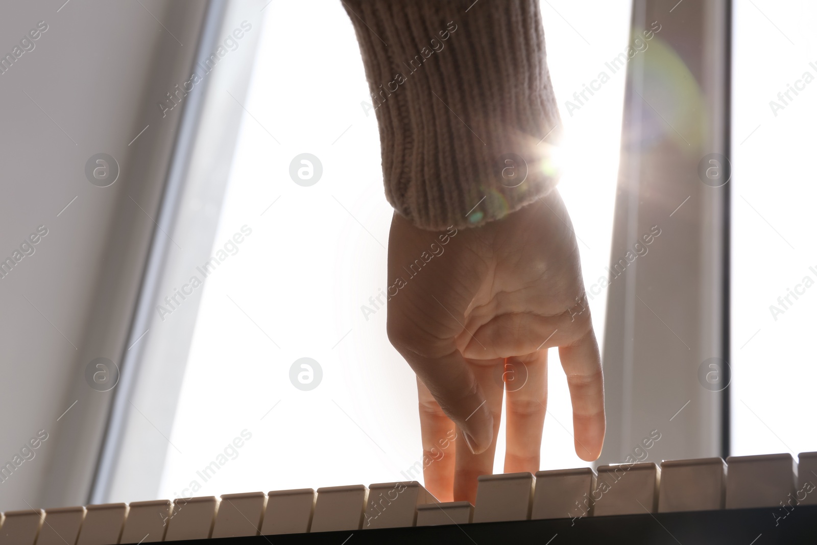 Photo of Young woman playing piano near window at home, closeup