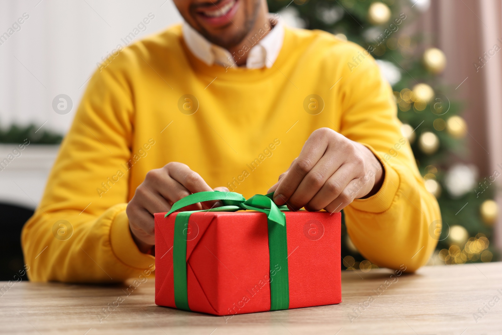 Photo of Man opening Christmas gift at wooden table in room, closeup