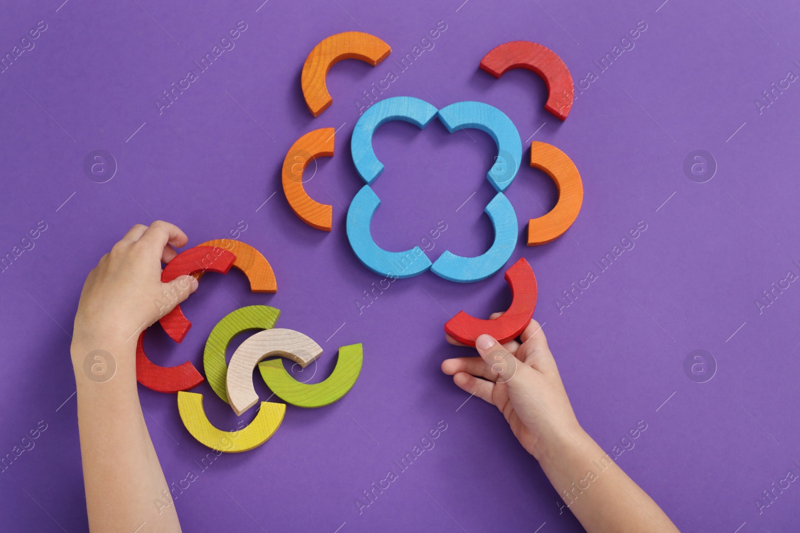 Photo of Motor skills development. Boy playing with colorful wooden arcs at purple table, top view