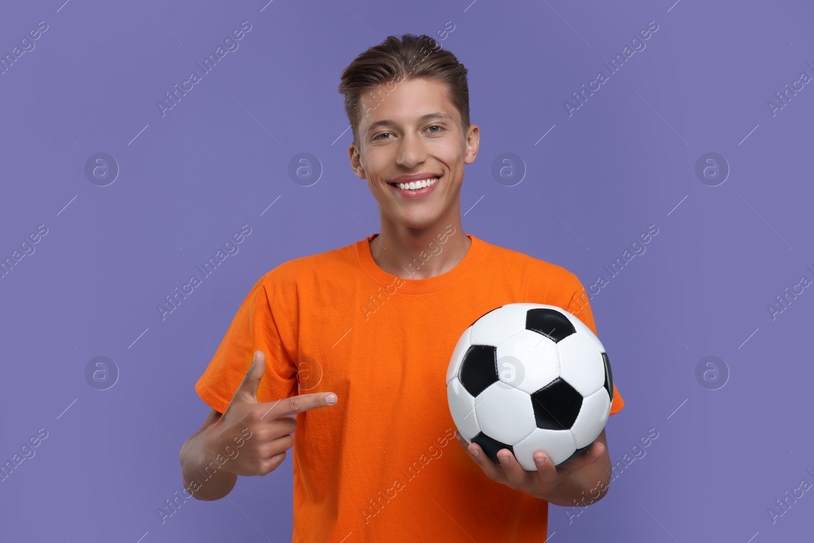 Photo of Happy sports fan pointing at soccer ball on purple background