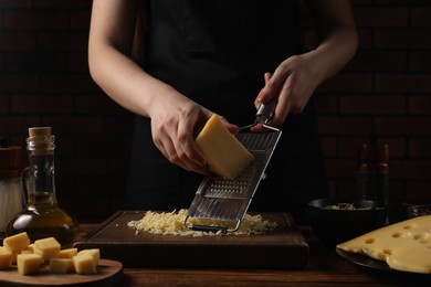 Woman grating cheese at wooden table, closeup