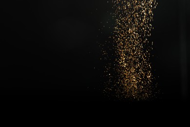 Photo of Shiny golden glitter falling down on black background, space for text. Bokeh effect