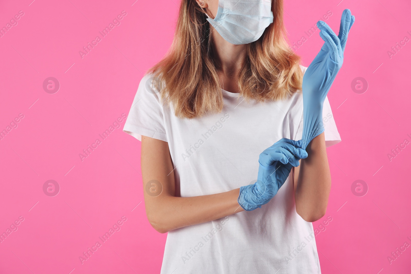 Photo of Young woman in protective mask putting on medical gloves against pink background, closeup