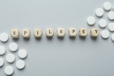 Photo of Word Epilepsy and pills on light grey background, flat lay