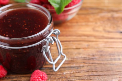 Photo of Jar of delicious raspberry jam and fresh berries on wooden table, closeup. Space for text